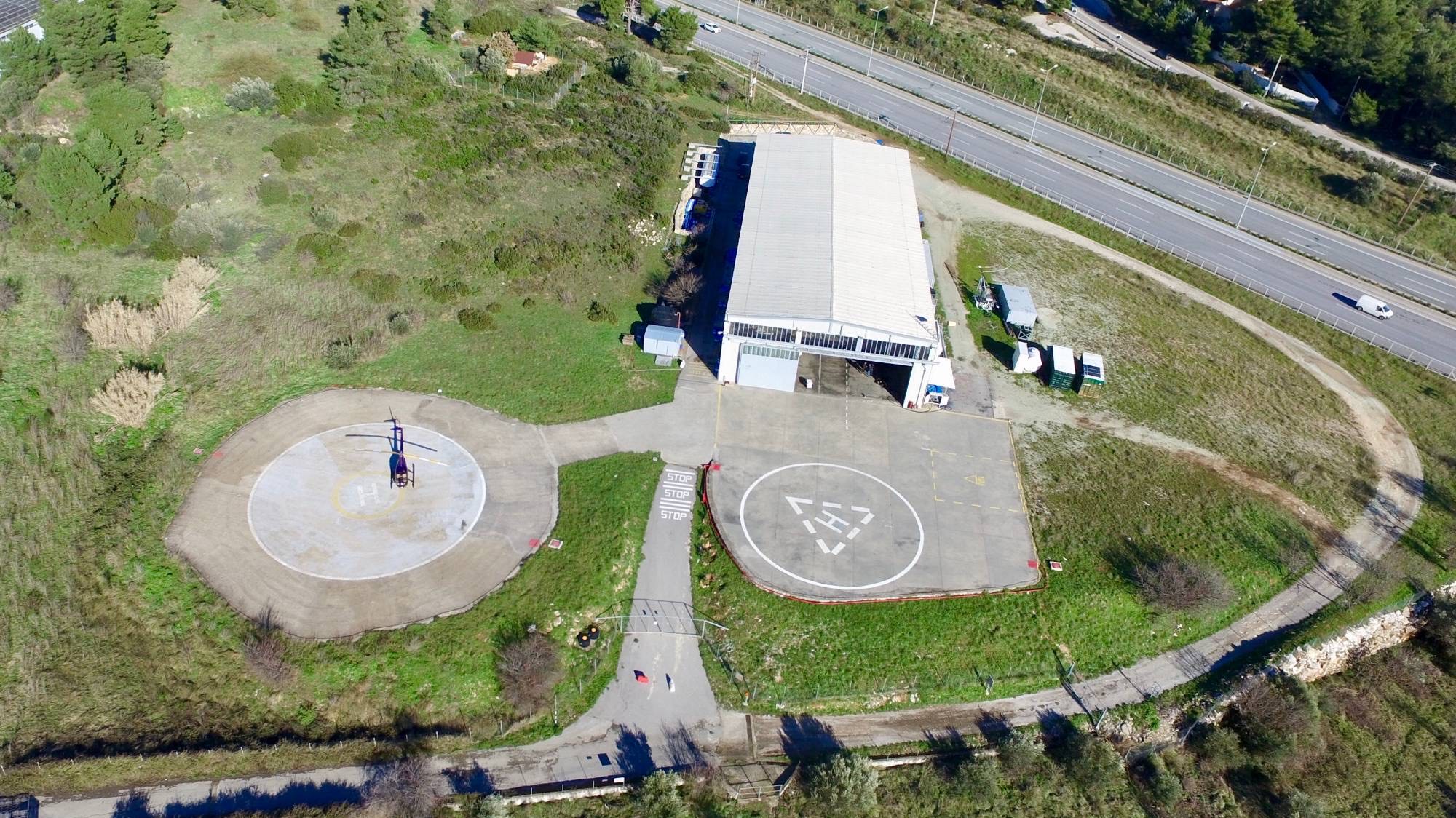 Aerial view of Athens Heliport: two helipads, the hangar, a fire-fighting water tank and refuel containers beside the Athens–Lamia National Road